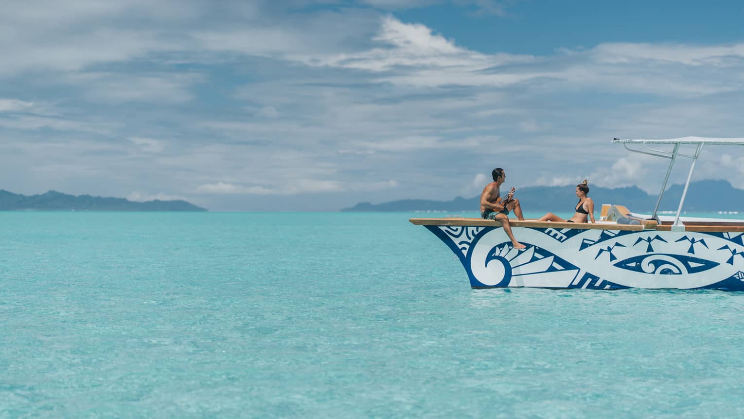 Man plays ukulele for woman on catamaran boat on lagoon