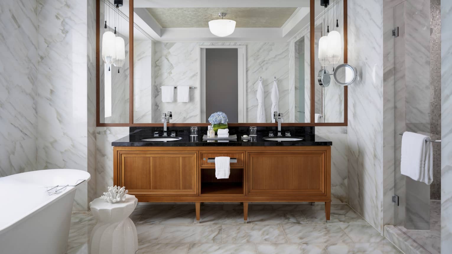 Large bathroom with marble floors and walls, wooden vanity and freestanding tub