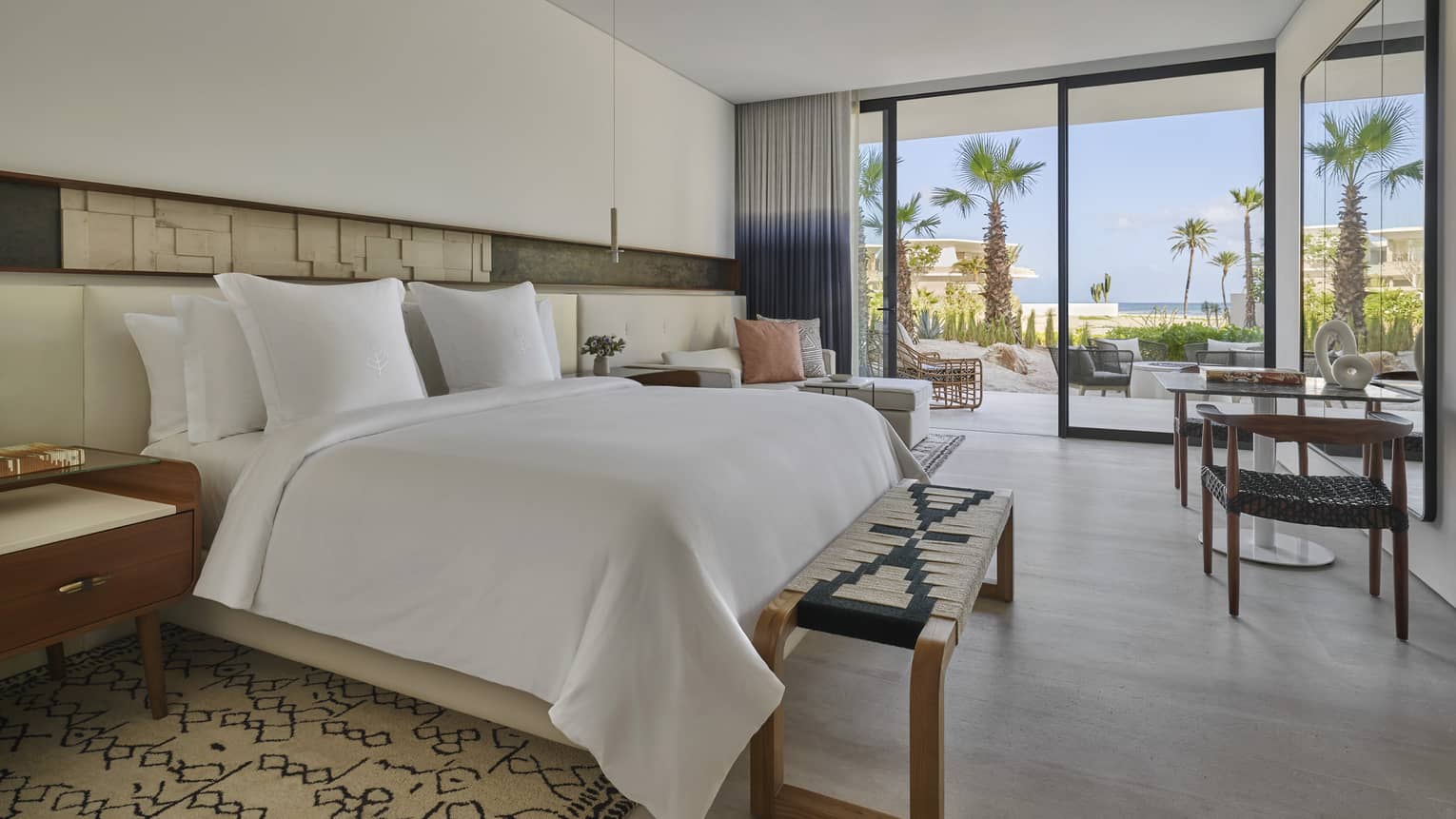 Bedroom with white king bed, woven bench, grey wood floors, walk-out private terrace