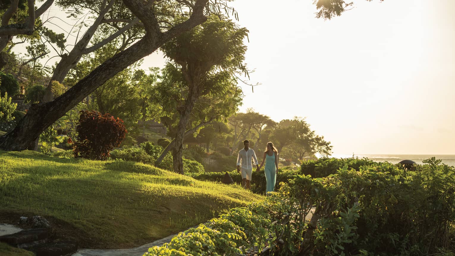 Couple walking hand-in-hand along pathway through beachfront garden