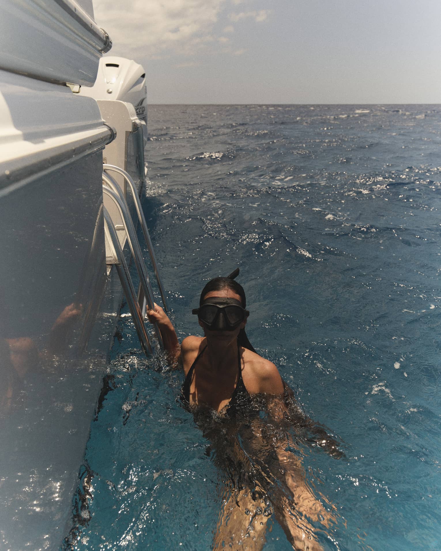 A woman wearing snorkelling goggles holds onto edge of boat in the water