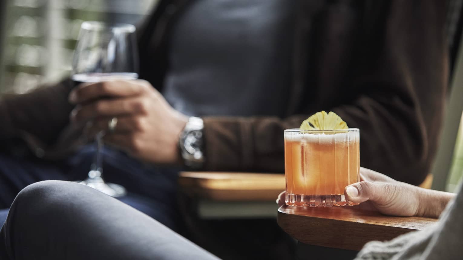 Close-up of two people sitting, holding cocktail and glass of wine