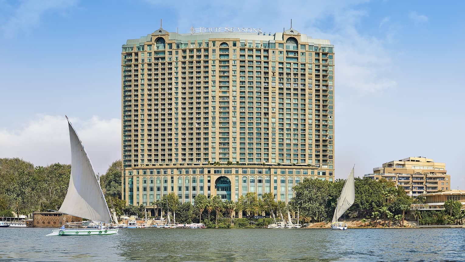Exterior shot of a large hotel building on the water, sail boats can be seen in the foreground.