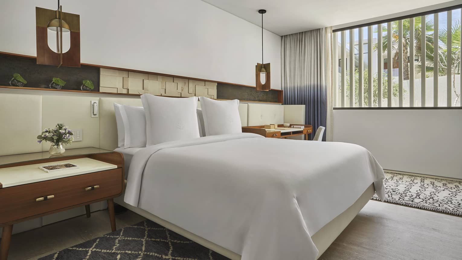 Two Bedroom Ocean View Suite with King bed, white linens, grey and white accent rugs, full-length headboard, cherry oak side table, window with two-tone curtains