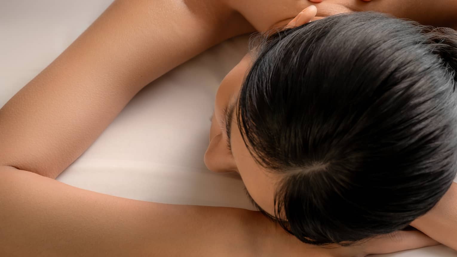 Two hands apply gentle pressure on the bare upper spine of a guest lying on their stomach on a massage table.