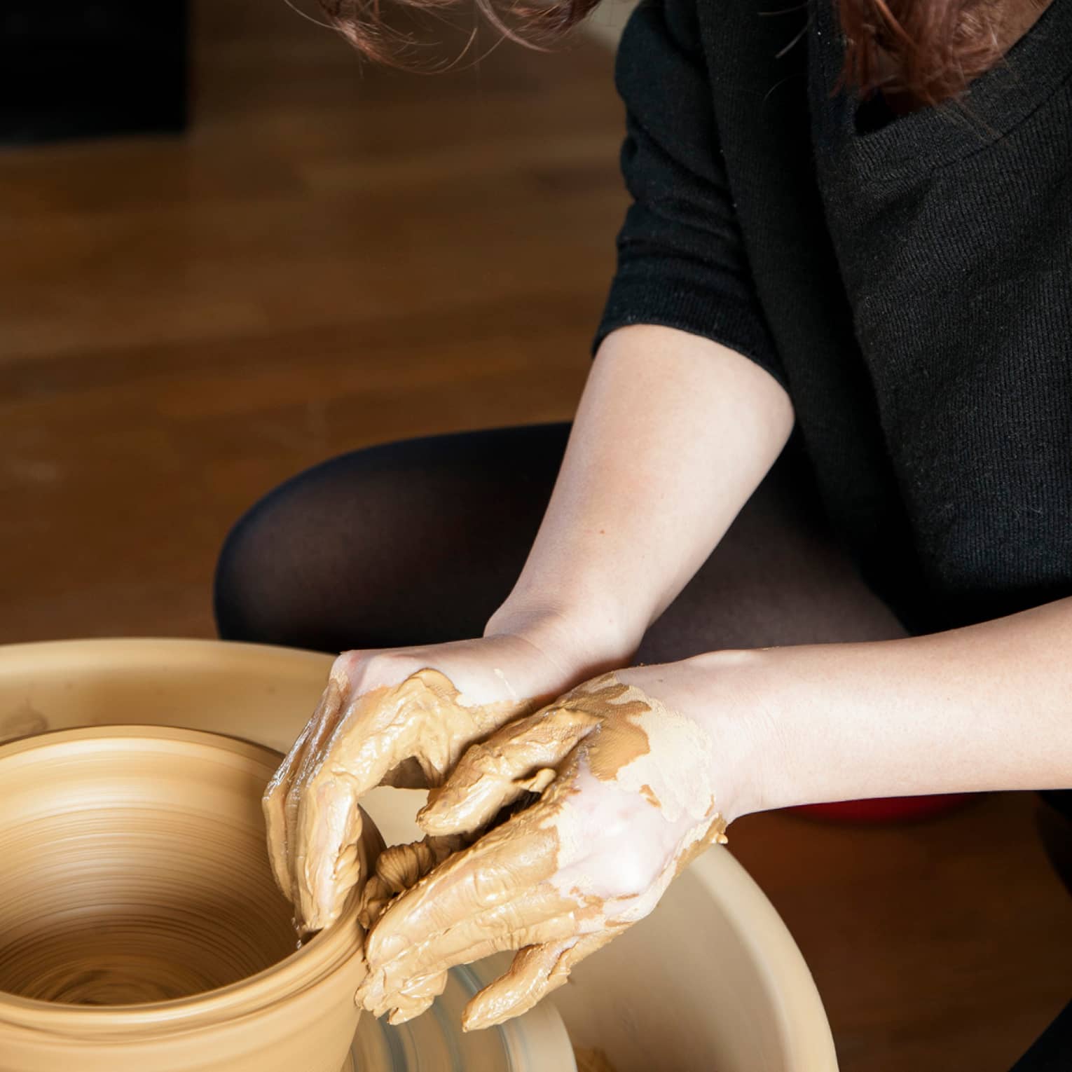 Close-up of hands covered in clay making pottery
