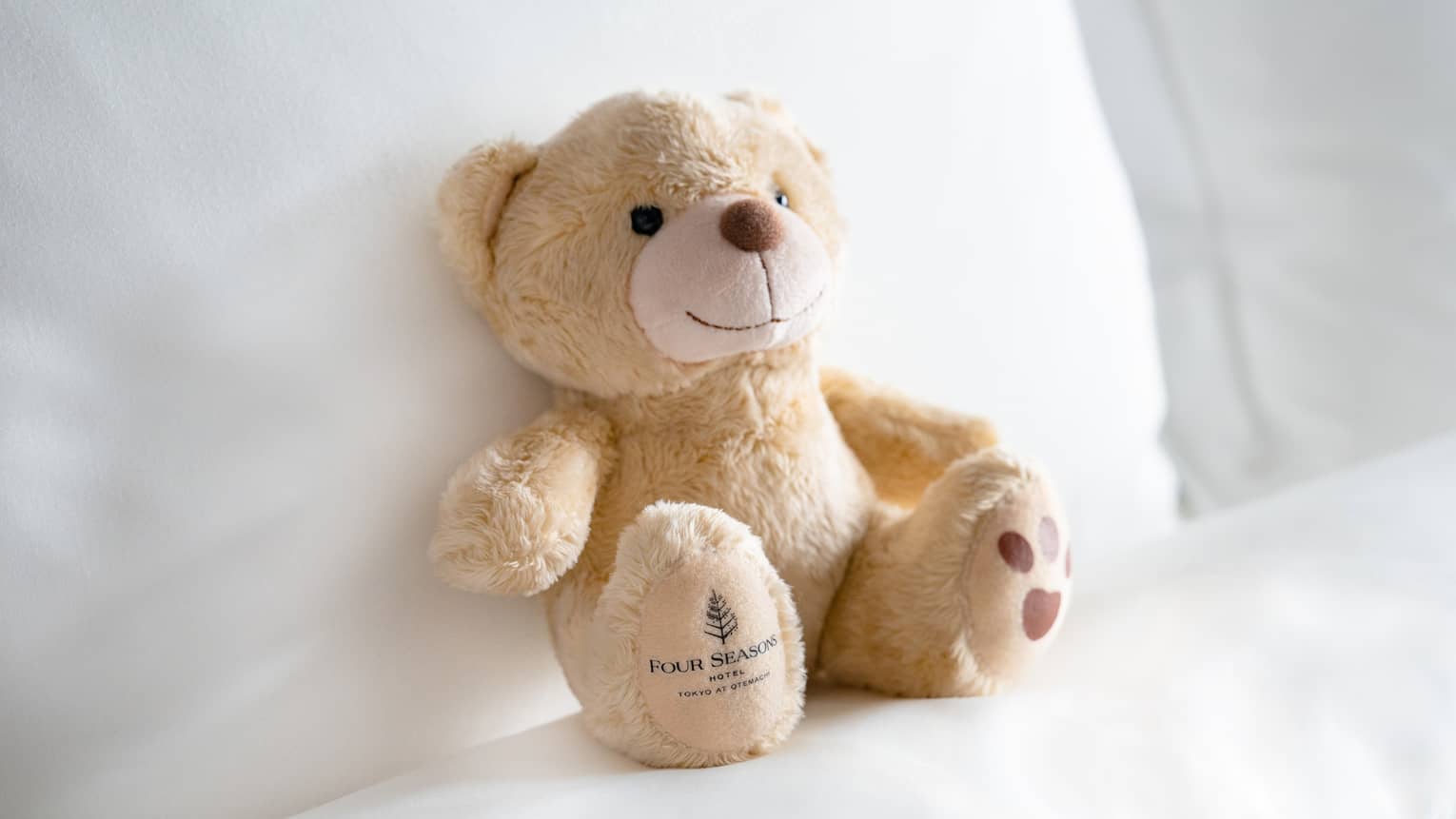 FS Otemachi teddy bear propped up on pillow with white linens