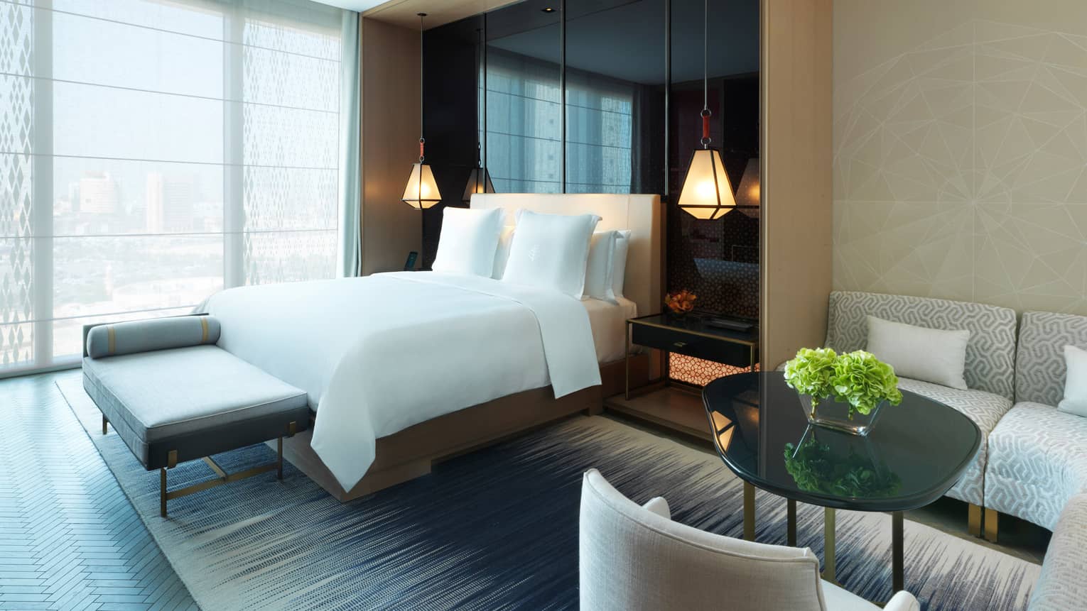 Deluxe Room small dining table, bed, modern chaise at foot in front of sunny floor-to-ceiling window