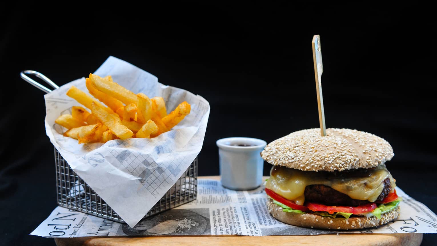 A burger with lettuce, tomato and cheese sits on a tray next to a basket of french fries
