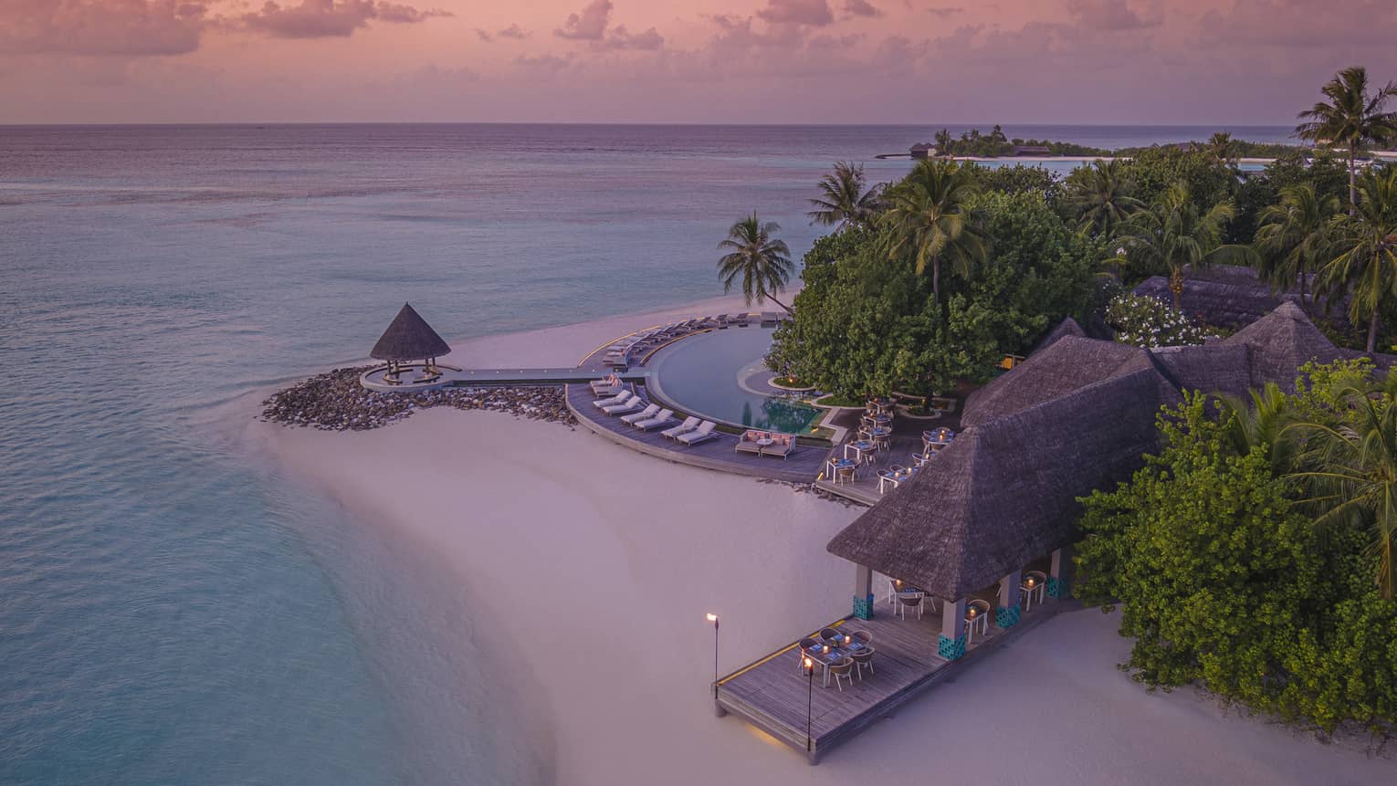 Aerial view of beachfront straw roof pavilion at sunset