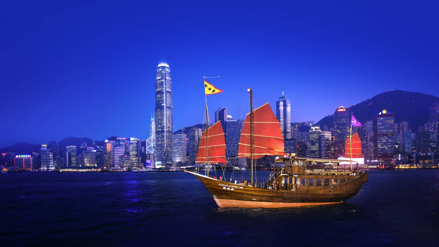 Ship with red sails cruises along the water with views of downtown in the background and clear blue sky