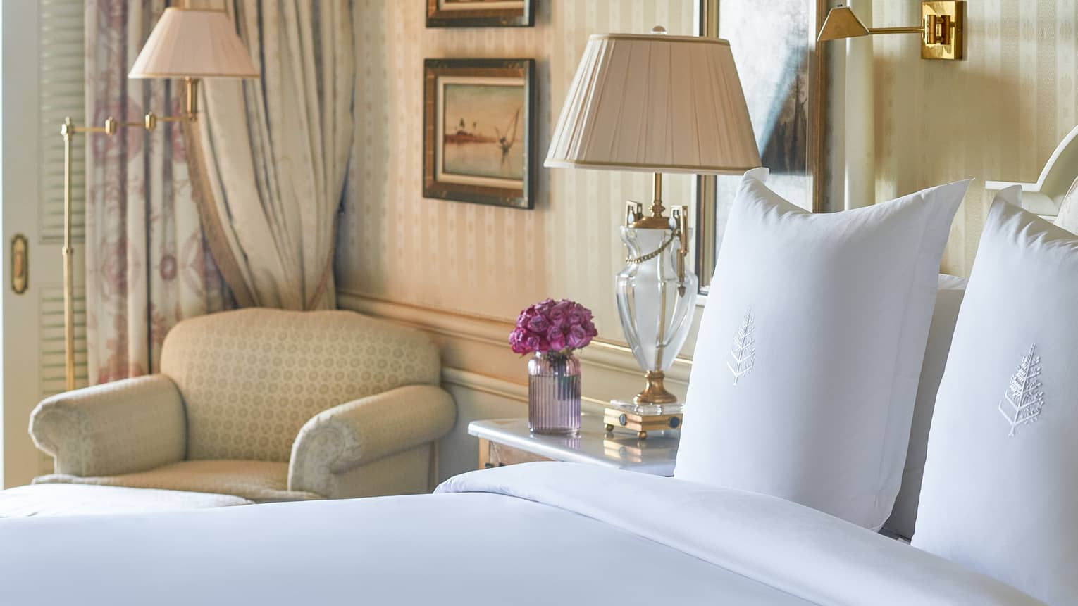 Close-up of bed with white linens, corner armchair, side table