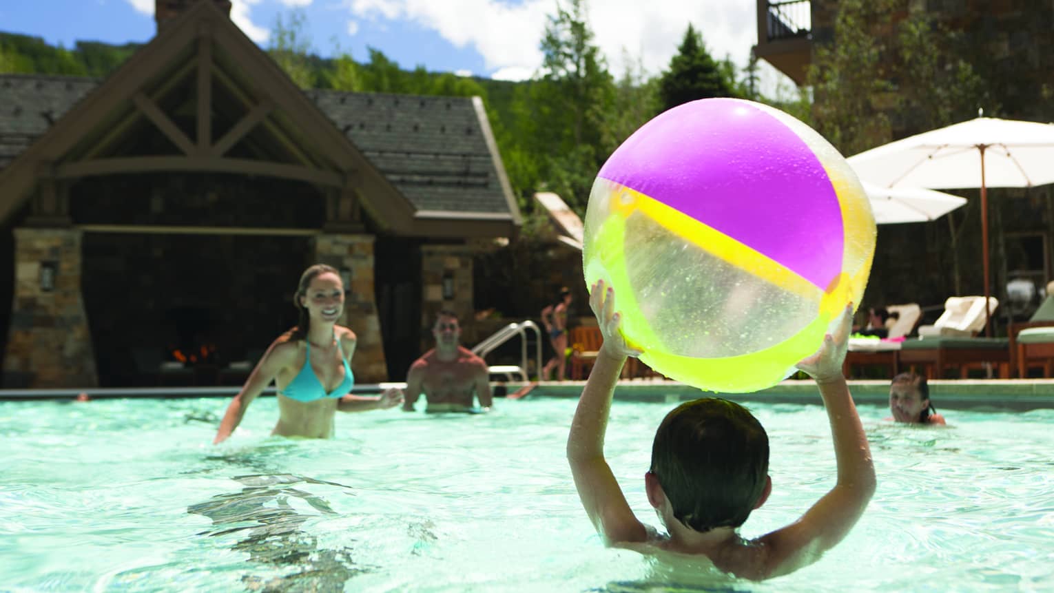 A group of children and young people playing with a beach ball in an outdoor pool.