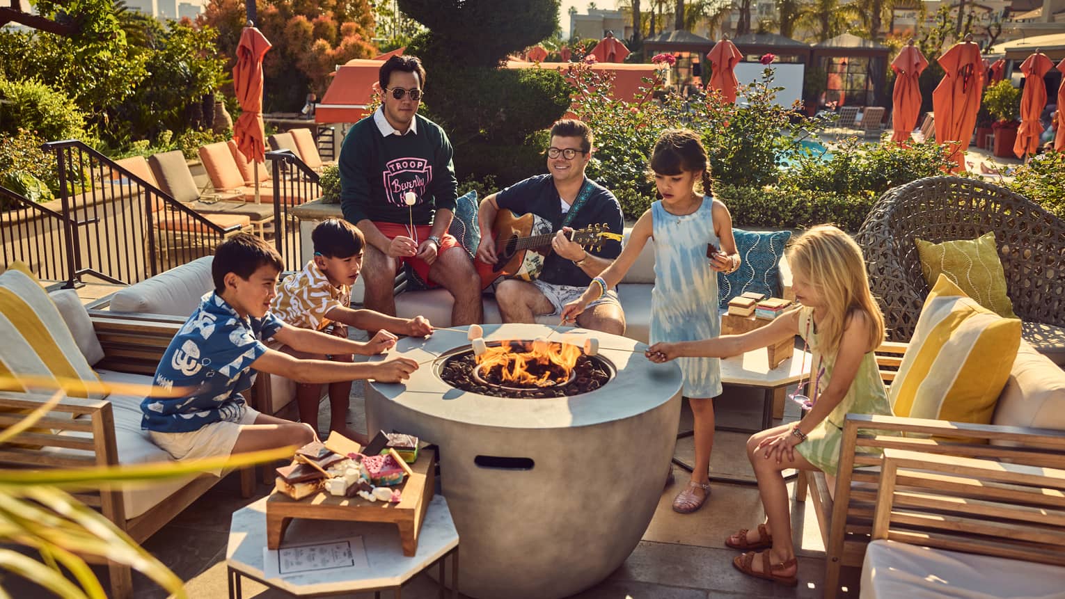 Young guests roasting marshmallows by a fire pit while a person plays the guitar