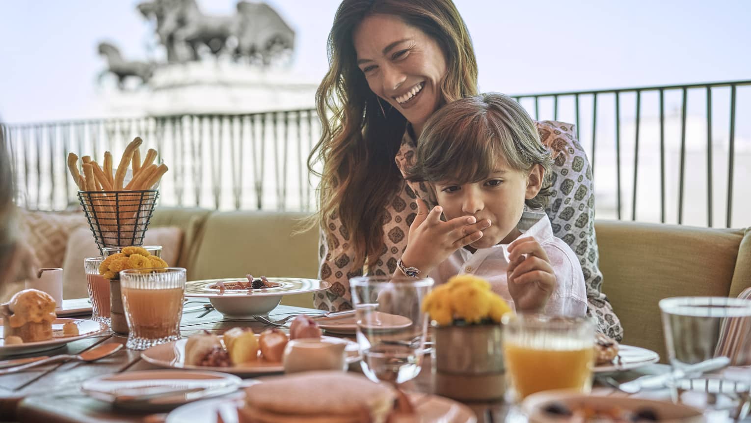 Woman and young boy sit at outdoor restaurant table with food