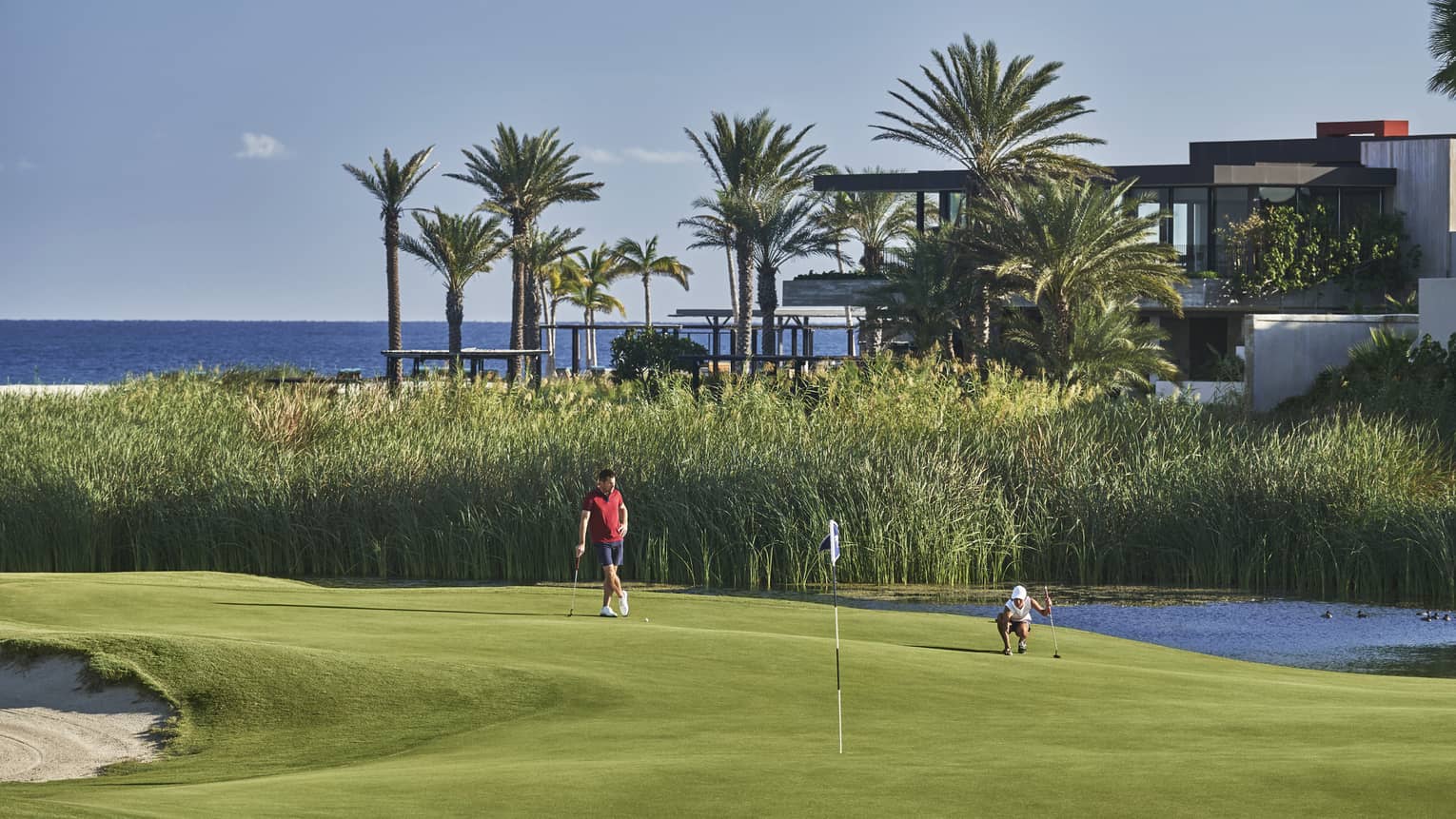 Two golfers enjoy a day on the golf course at four seasons Los Cabos with palm trees and the ocean in the background