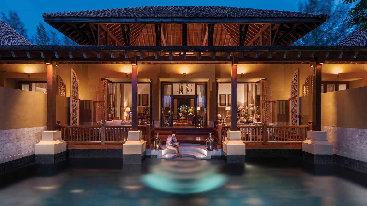 Woman sits on edge of pool off steps to Family Garden Villa at night