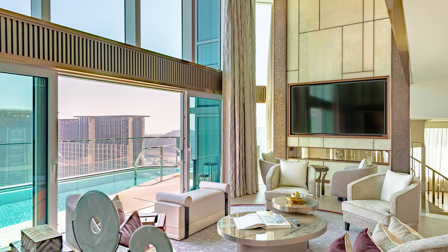 A spacious, stylish living room with sliding doors opening onto a private pool that overlooking a cityscape. 