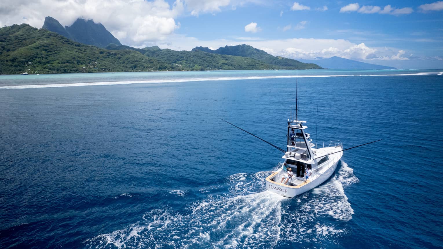 Yacht creates wake in water as it heads out to open sea, lush green mountains in background