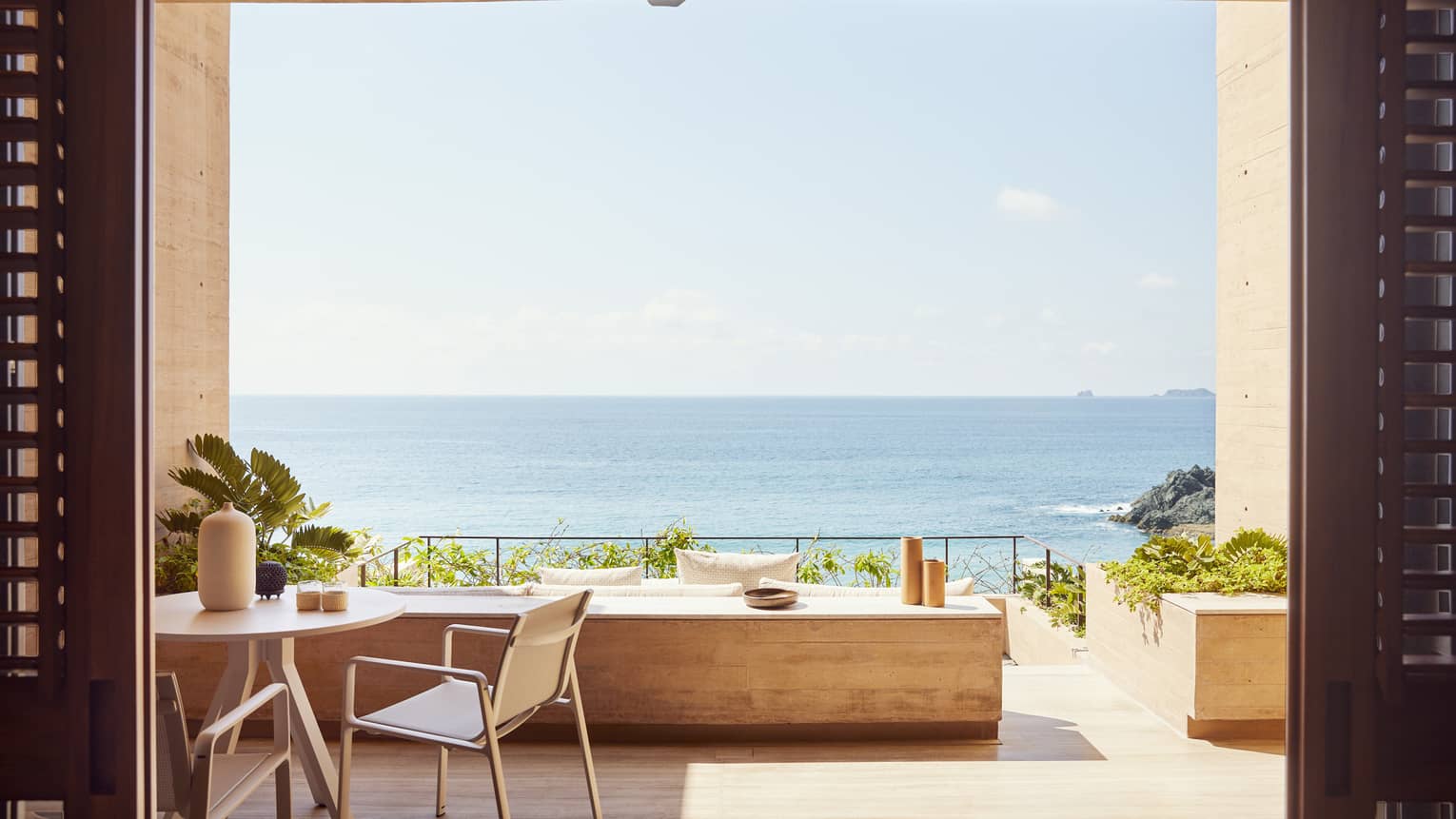 The exterior of a beachfront room with a small table and a large opening looking out at an ocean.