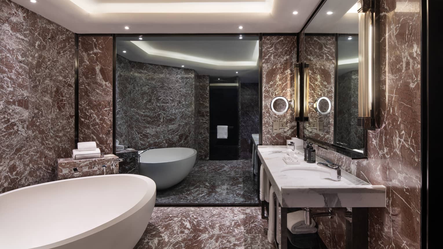 Guest room bathroom with chocolate marble accents, large soaking tub, double vanity with lighted wall sconces