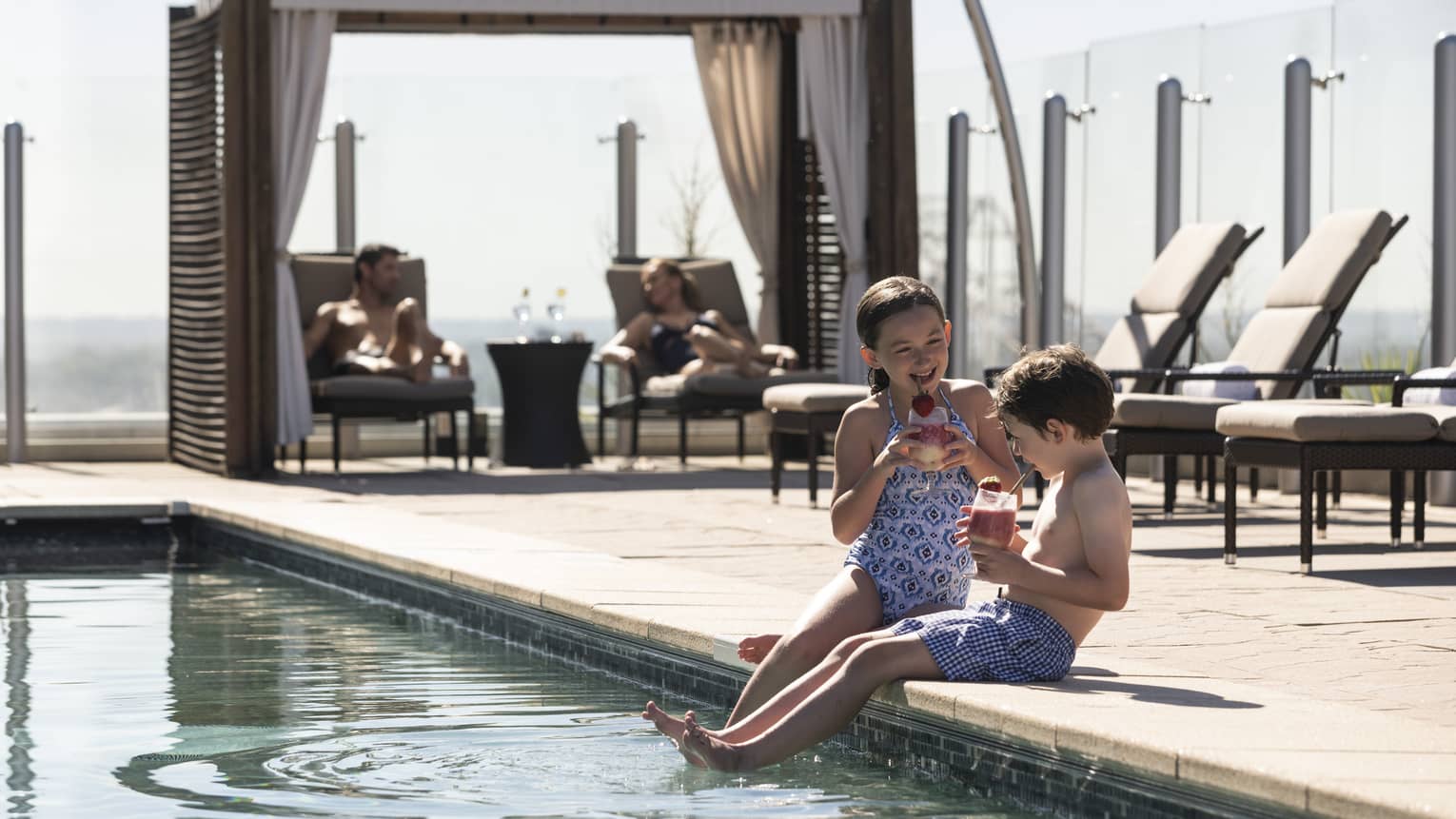 Two children sitting next to a pool with their feet int he water.