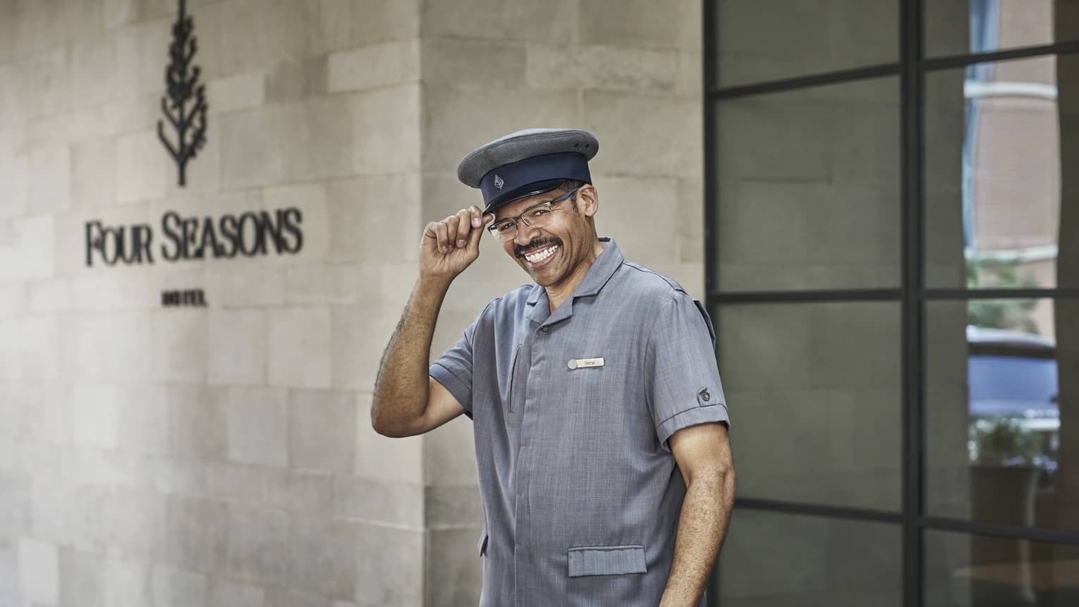A smiling doorman greets guests outside of the Hotel