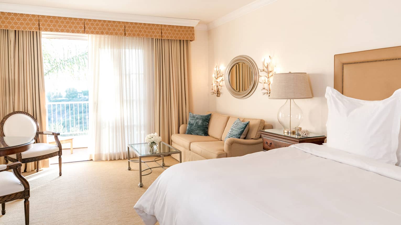 Hotel villa bedroom, bed and seating area by sunny floor-to-ceiling patio door 