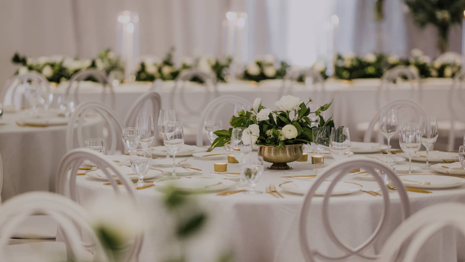 Round tables set for wedding reception with white linens and small floral centrepieces
