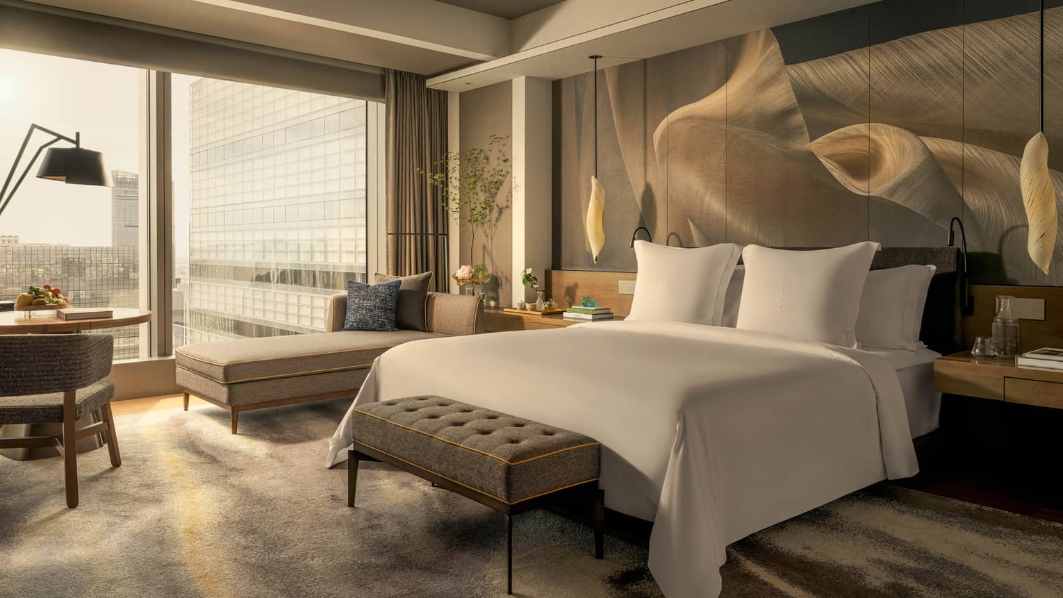 Luxury hotel room with king bed, chaise, hanging lights over bedside tables, and wall of windows