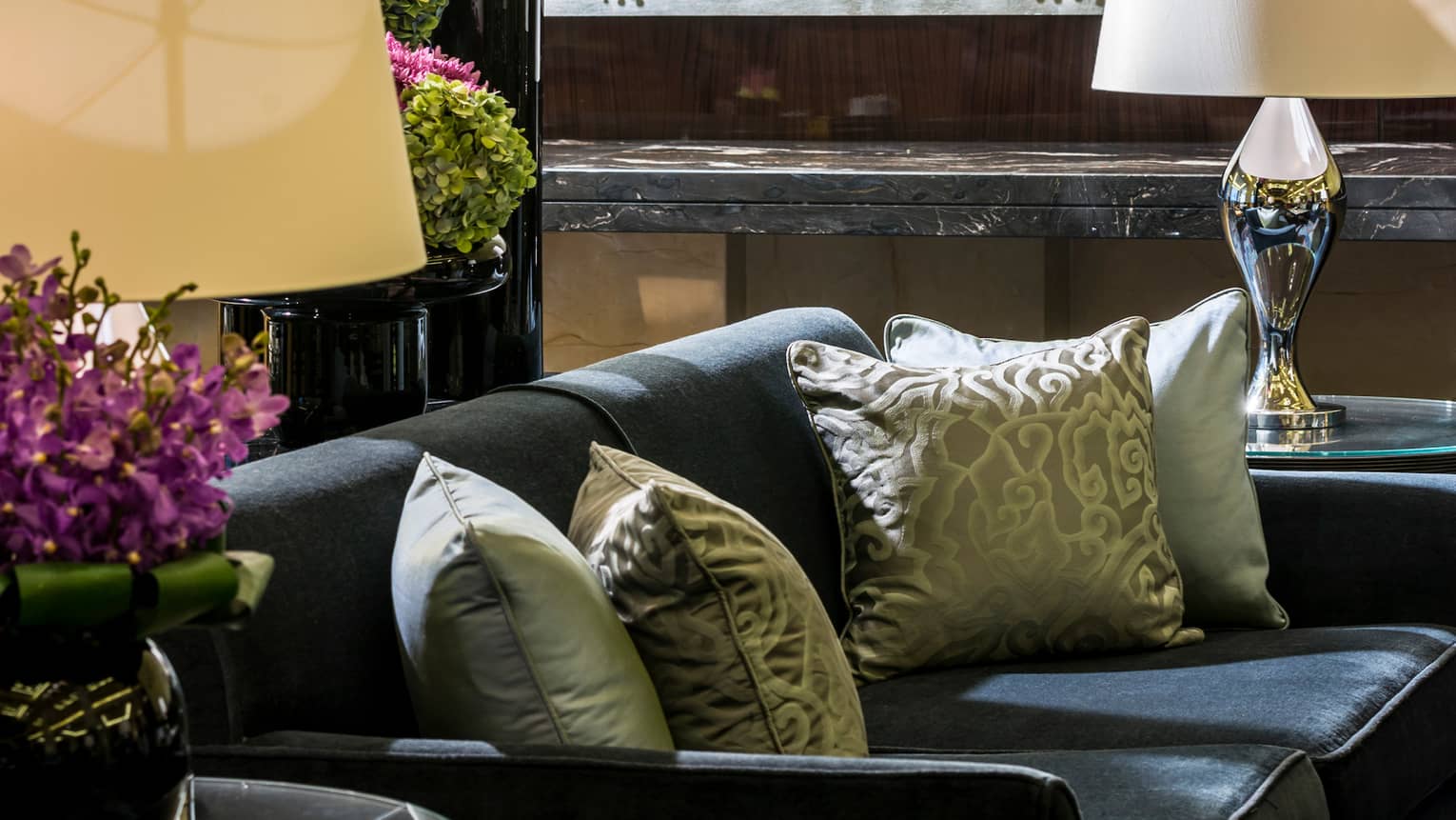 Close-up of Opus Lounge sofa with silver accent pillows, lamp on table, purple flowers