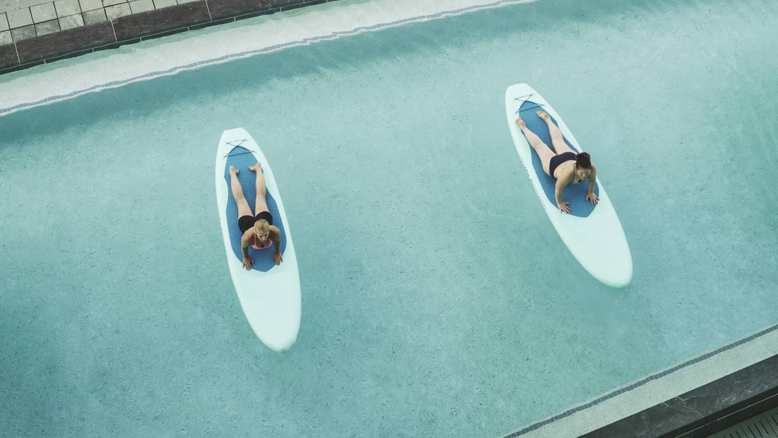 Aerial view of two people on paddleboards, floating on hotel swimming pool