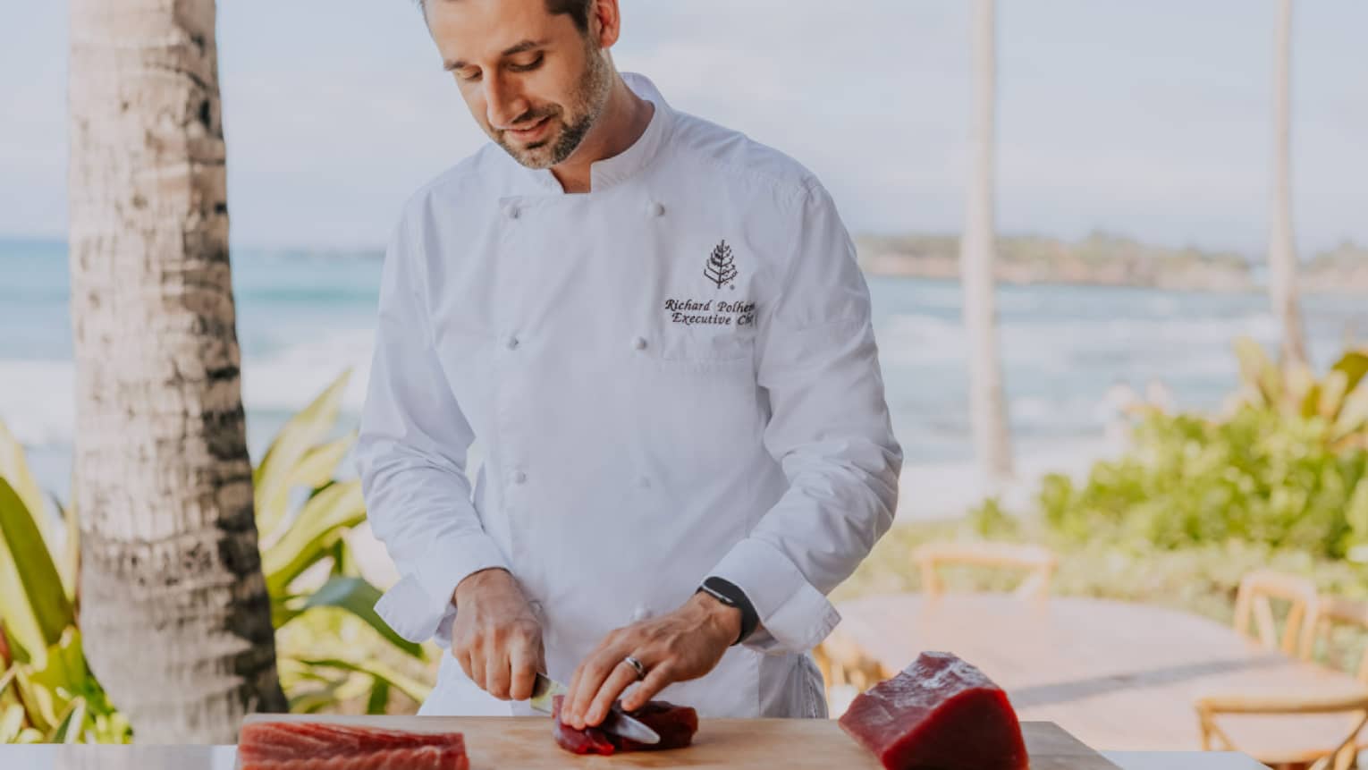 Male chef slices raw tuna on cutting board, beach in background