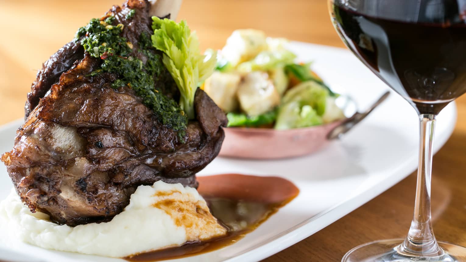 Close-up of roasted lamb chop on mashed potato, gravy and salad by glass of red wine