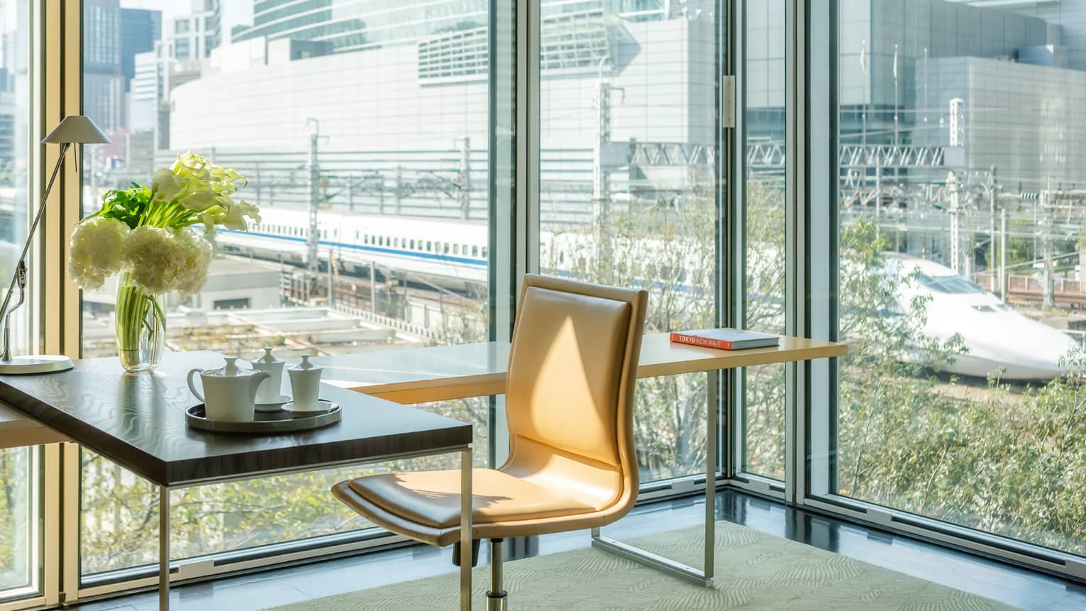 Modern seating area with a table set for tea and a vase with white flowers, overlooking large windows with a view of a high-speed train passing