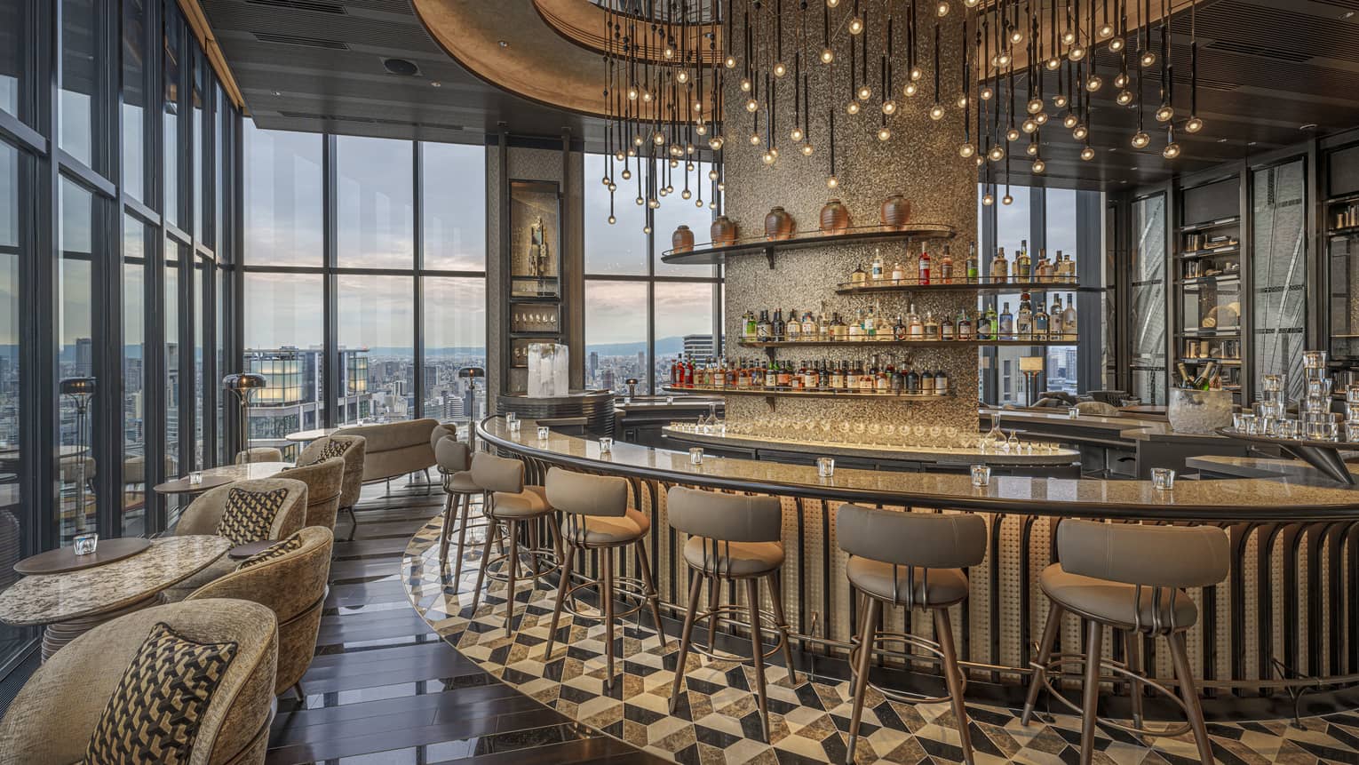 Large circular granite-topped bar in a modern luxury restaurant surrounded by a bank of windows overlooking city at dusk.