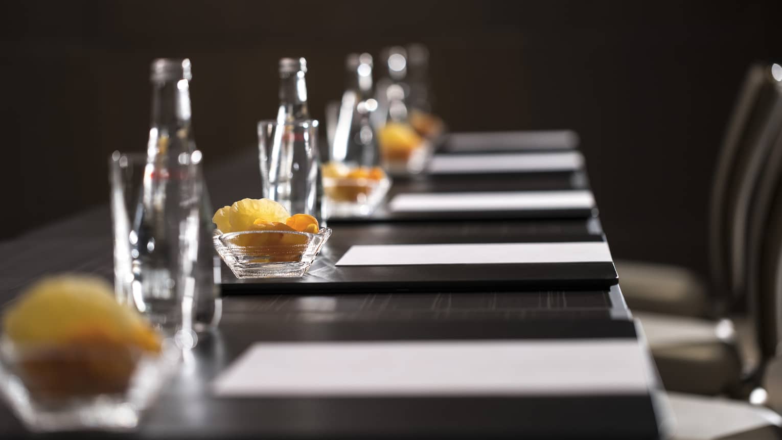 Row of glass bottles, small dishes with dried fruits, meeting agendas along boardroom table
