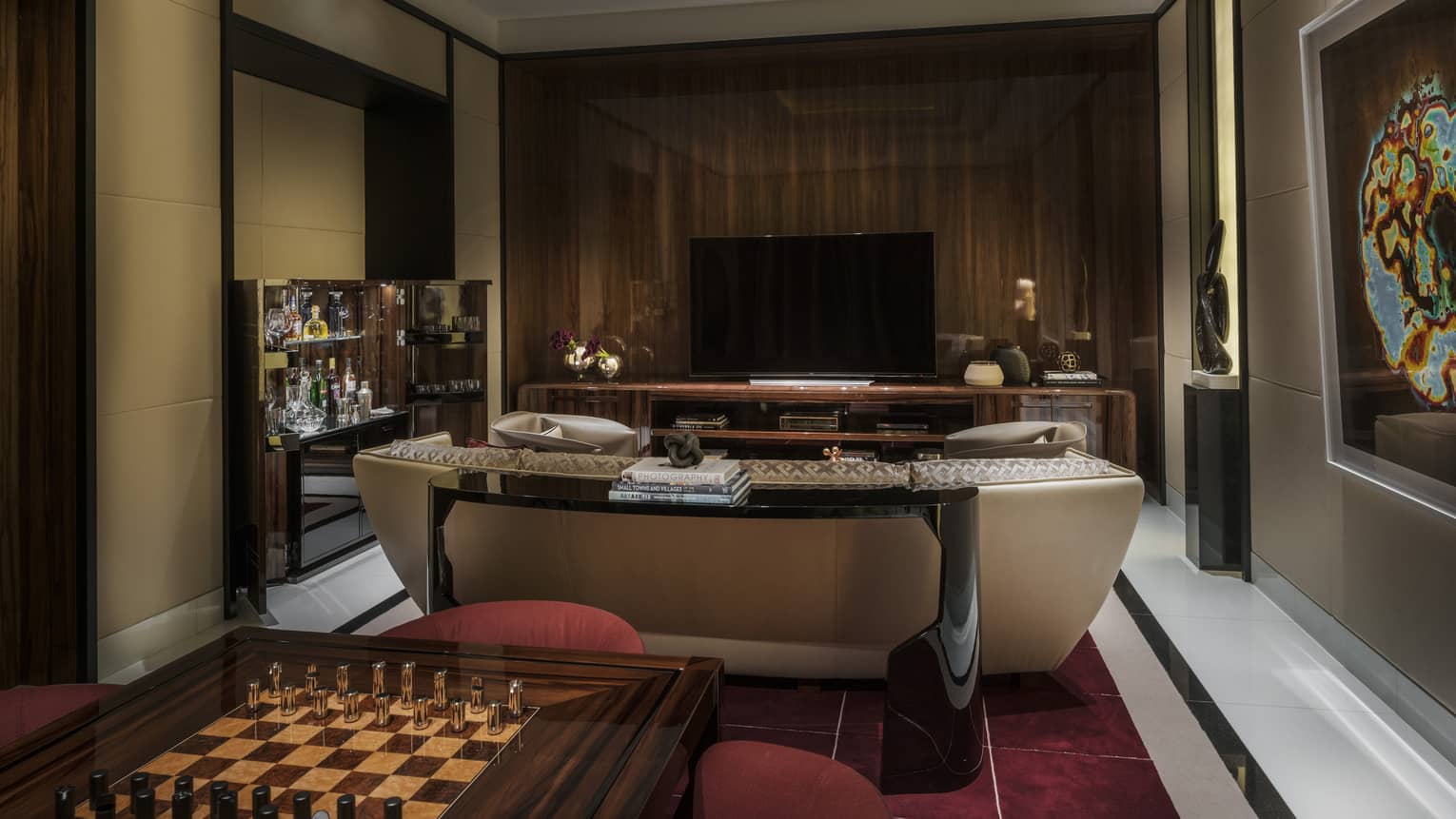 Private media room in a hotel suite with a large television, sofa, bar credenza and a chess table