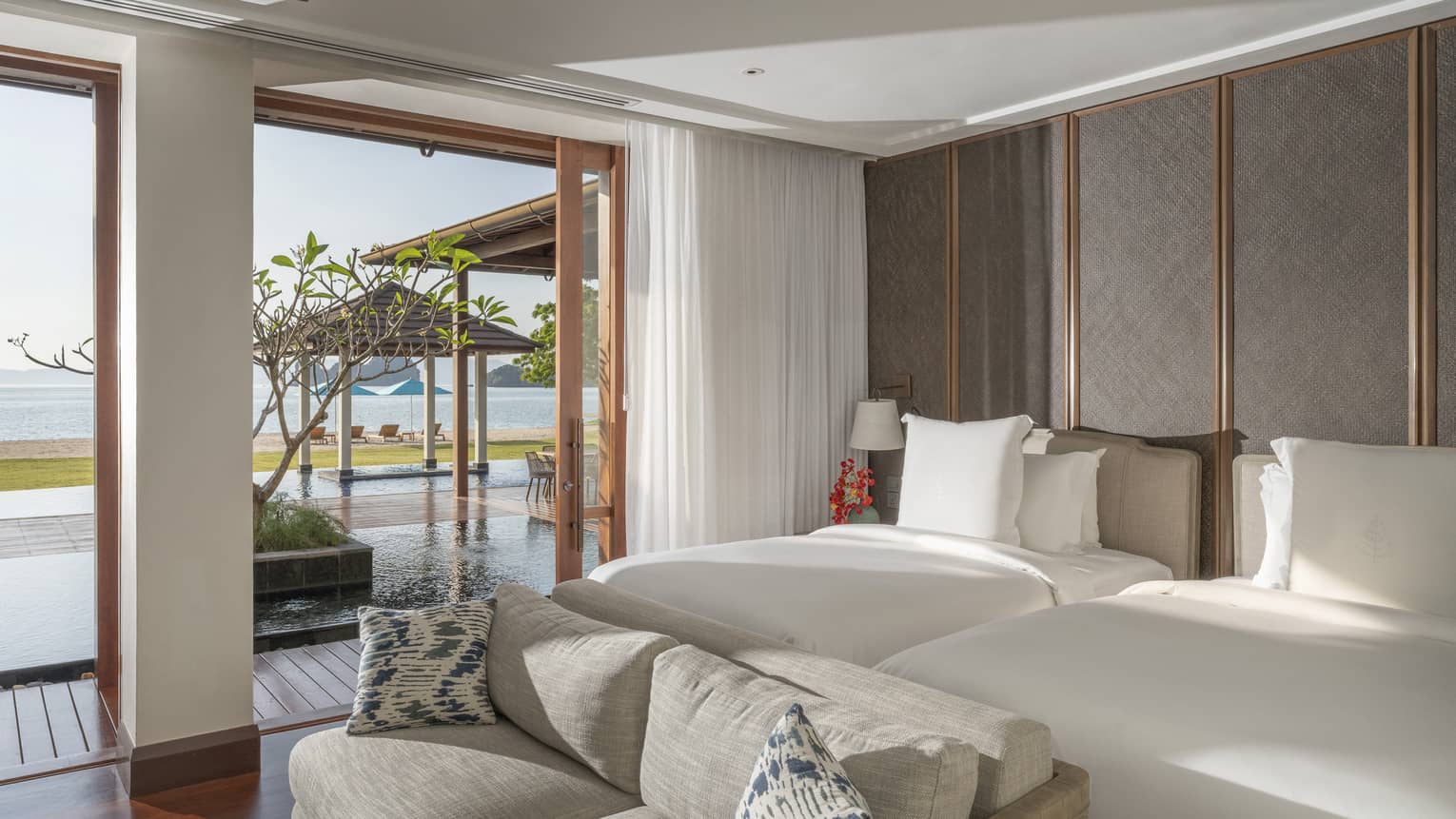Bedroom with two beds, sofa and walk-out terrace to the pool and beach view