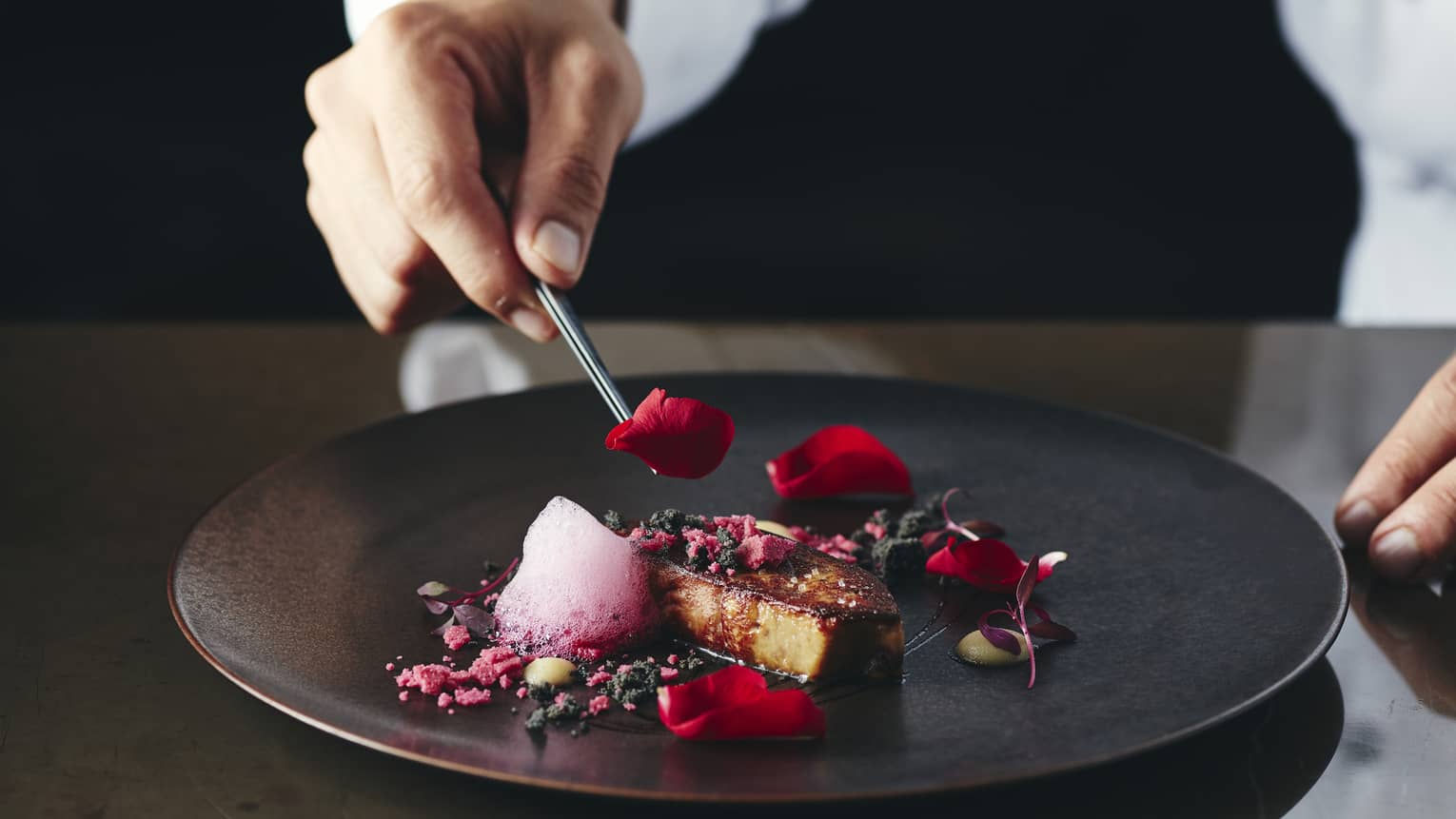 Chef places rose petal on small gourmet dessert