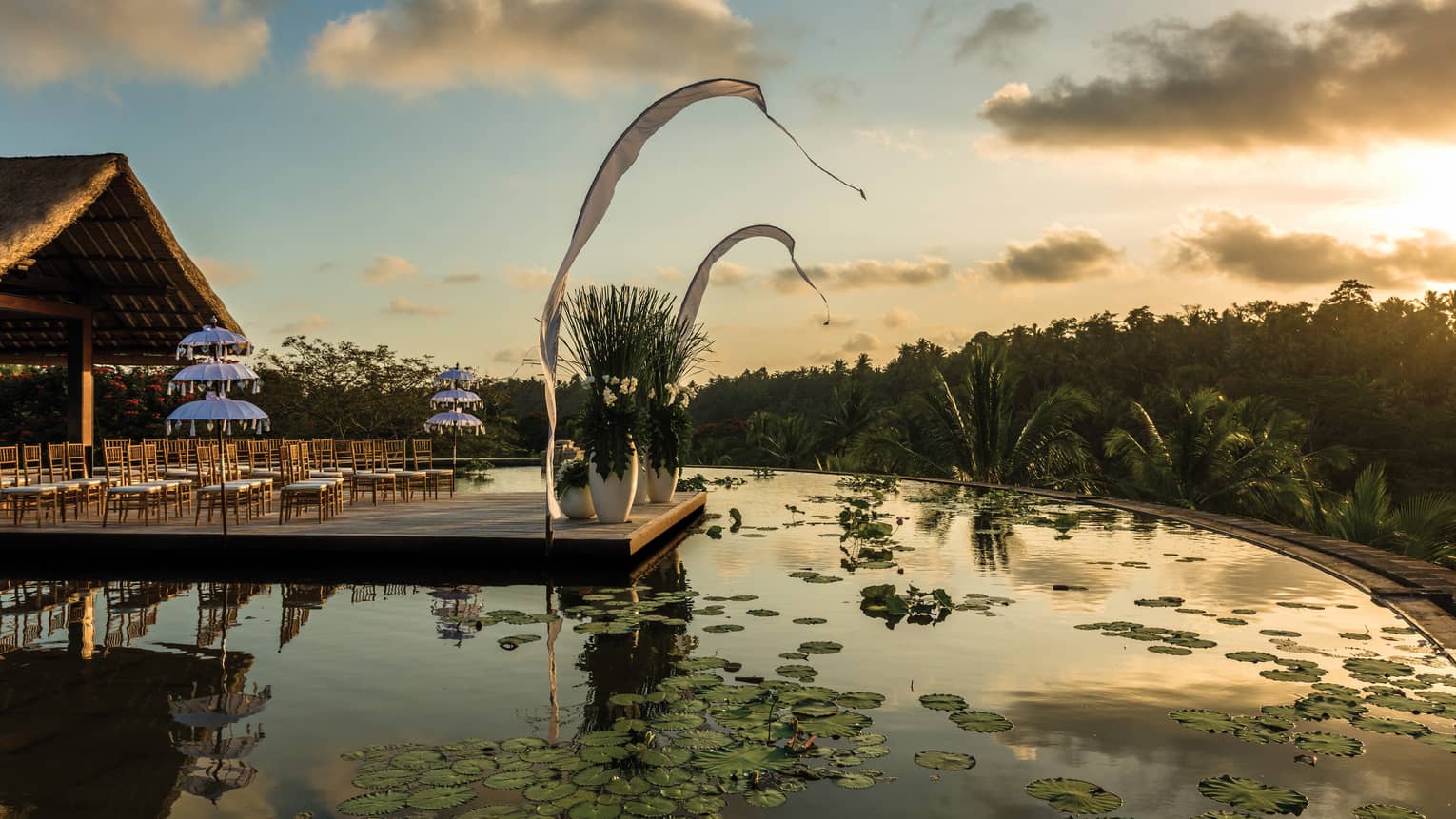 Rows of chairs set up for wedding ceremony on patio over lotus pond at sunset