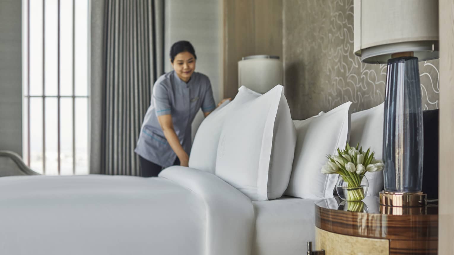 A room service attendant fluffing pillows on a freshly made bed