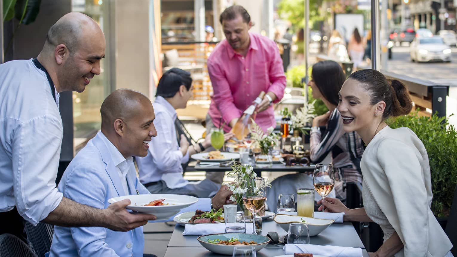A group of people eating on an outdoor terrace alongside a bustling city street