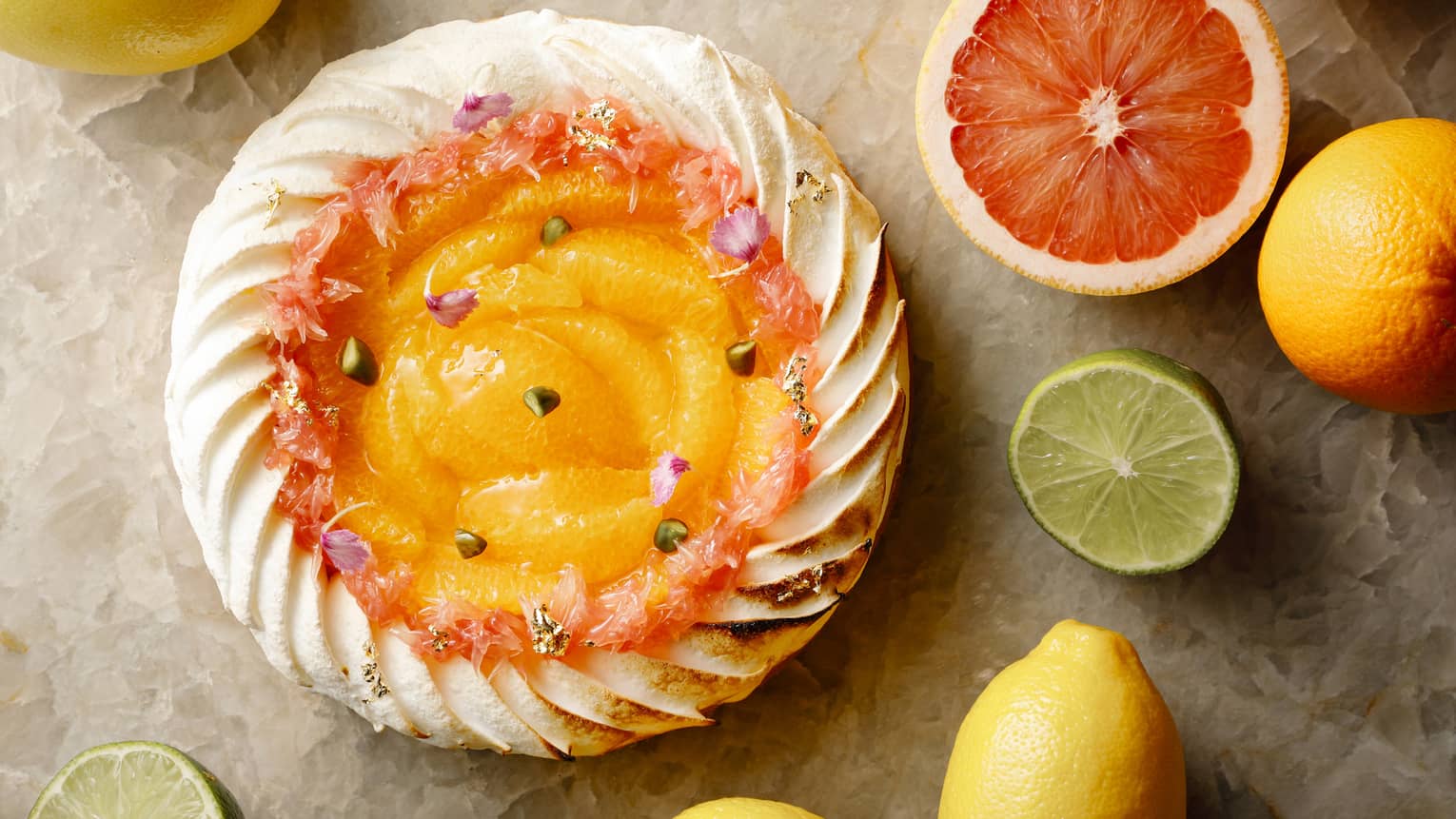 Aerial shot of whole citrus tart rimmed with pastry cream, halved citrus fruit on table surrounding it