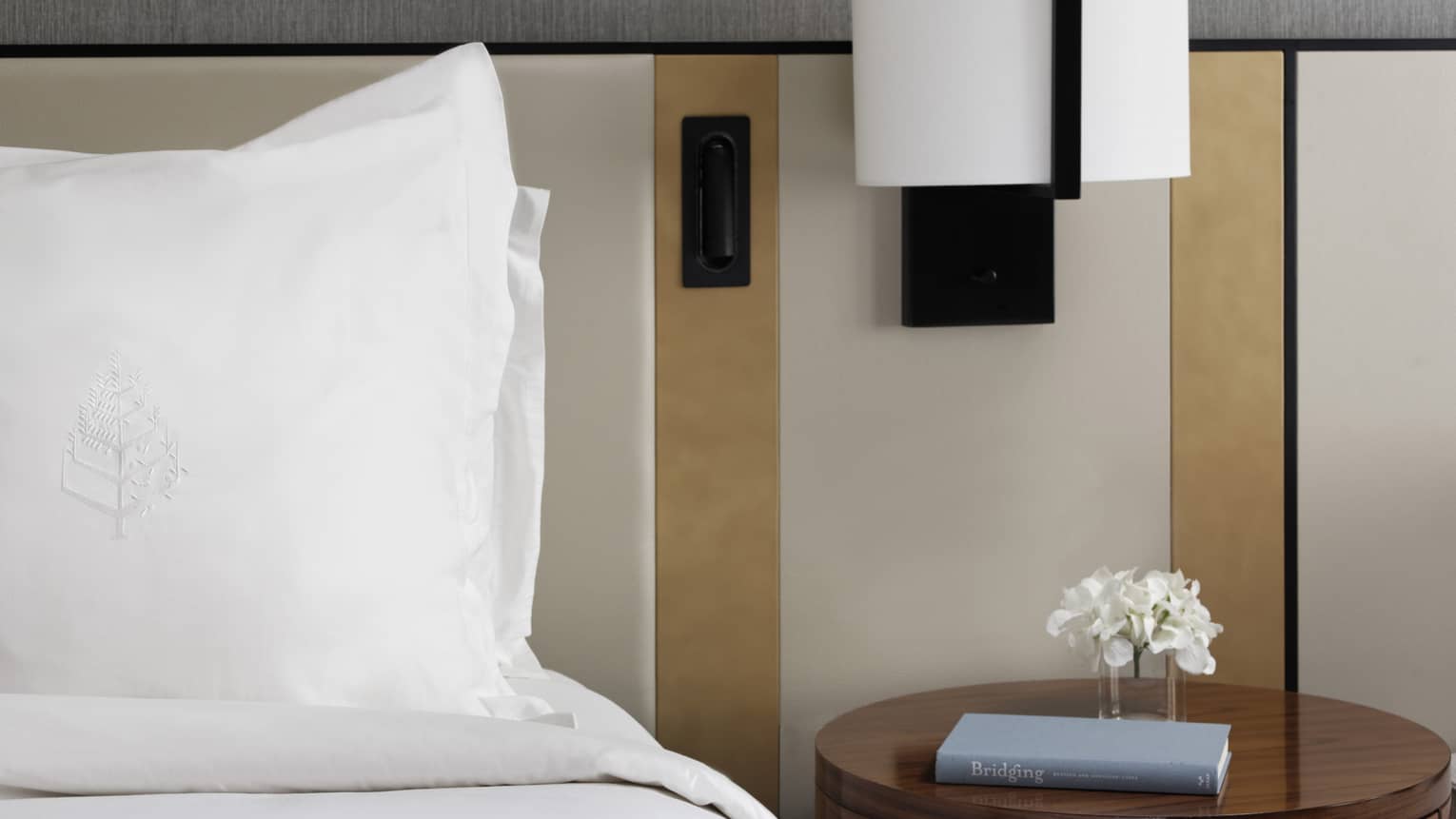 Bed with white linens, round side table with book, reading lamp