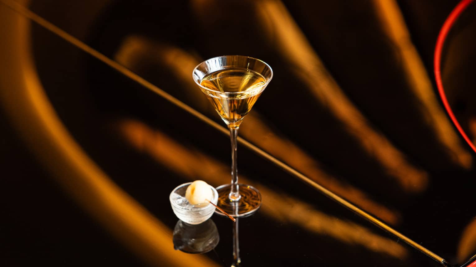 A martini glass on a polished surface holds a pale golden drink.