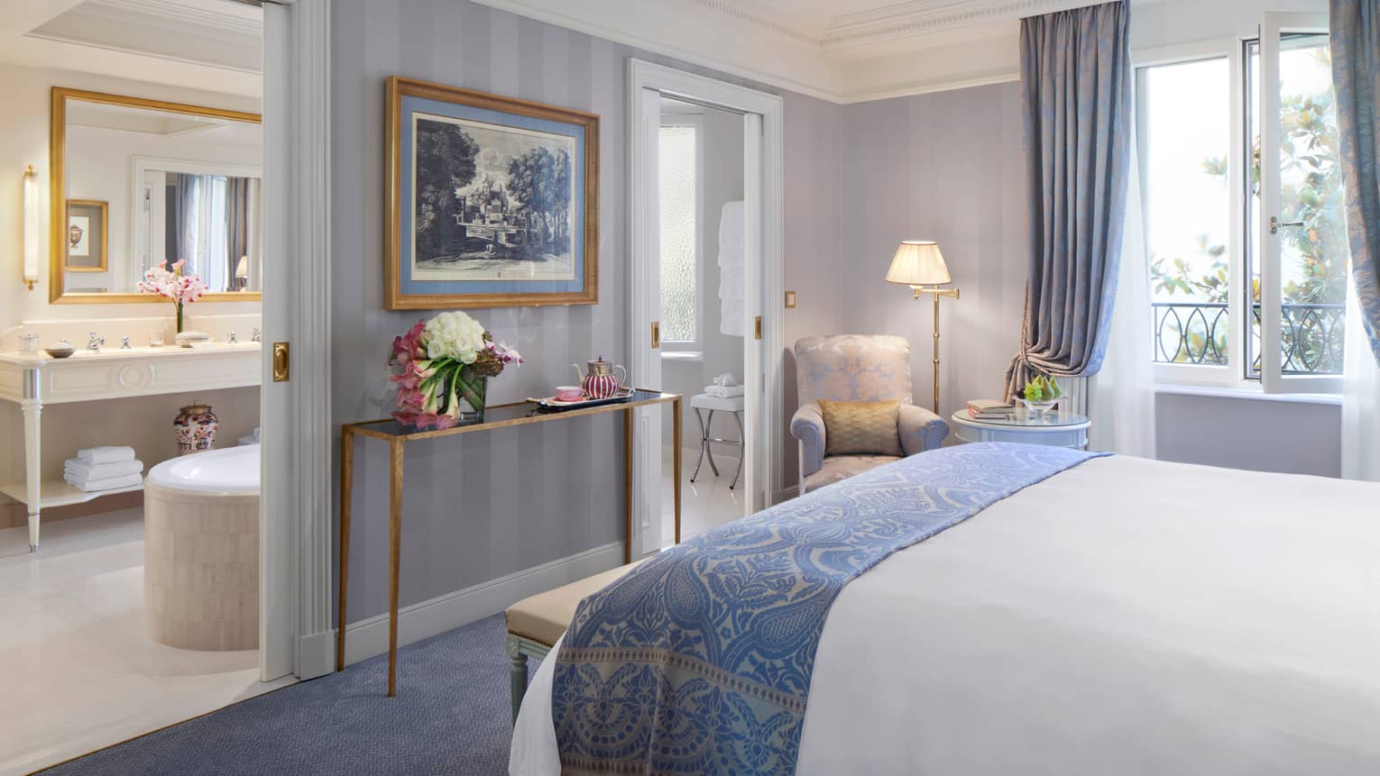 Superior Room end of bed with elegant folded blue blanket, table with fresh flowers, painting with gold frame, bathroom