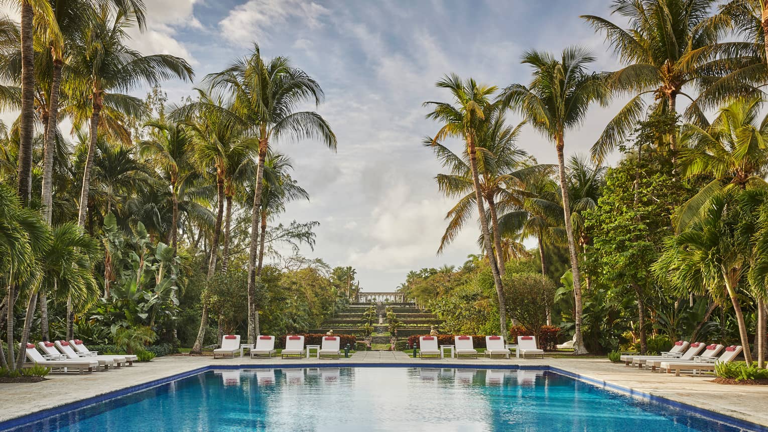 Luxury resort pool area with lounge chairs, surrounded by palm trees and lush greenery 
