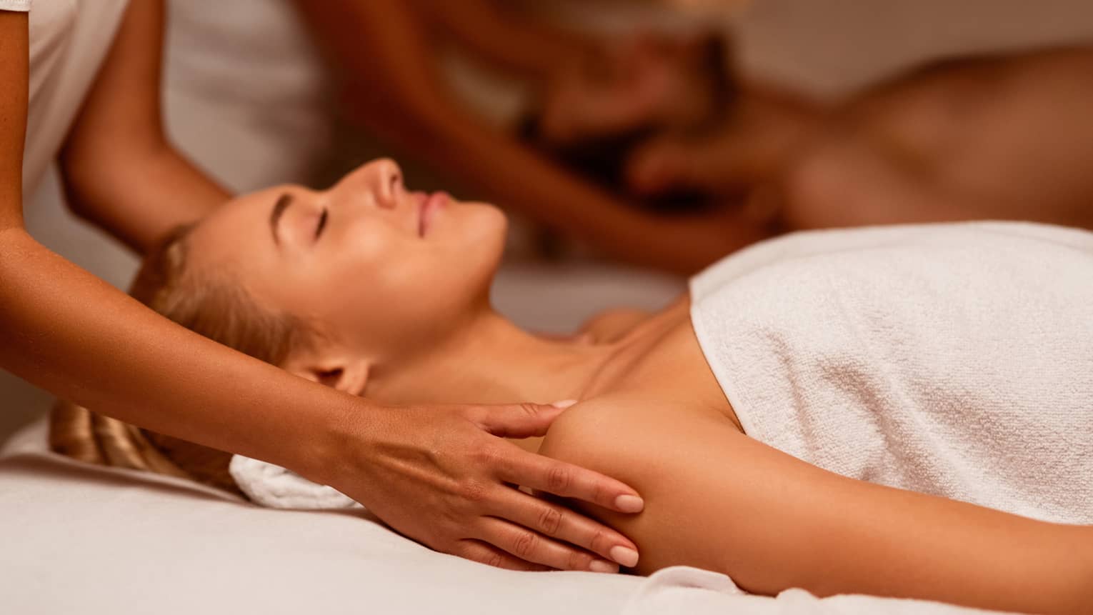 Two spa therapists perform a couples' massage