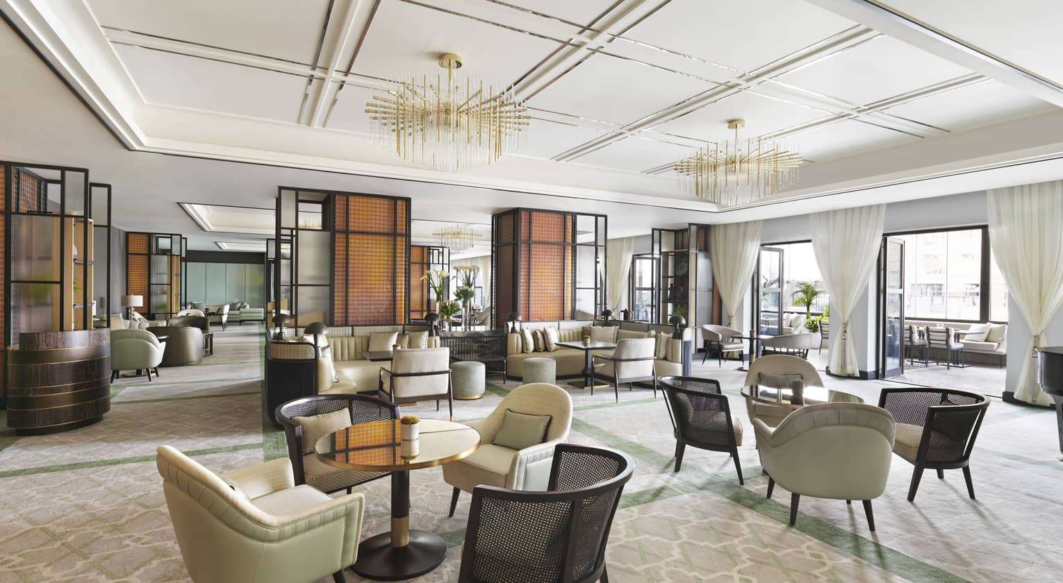 Interior of hotel lounge dining area featuring small round tables and upholstered chairs